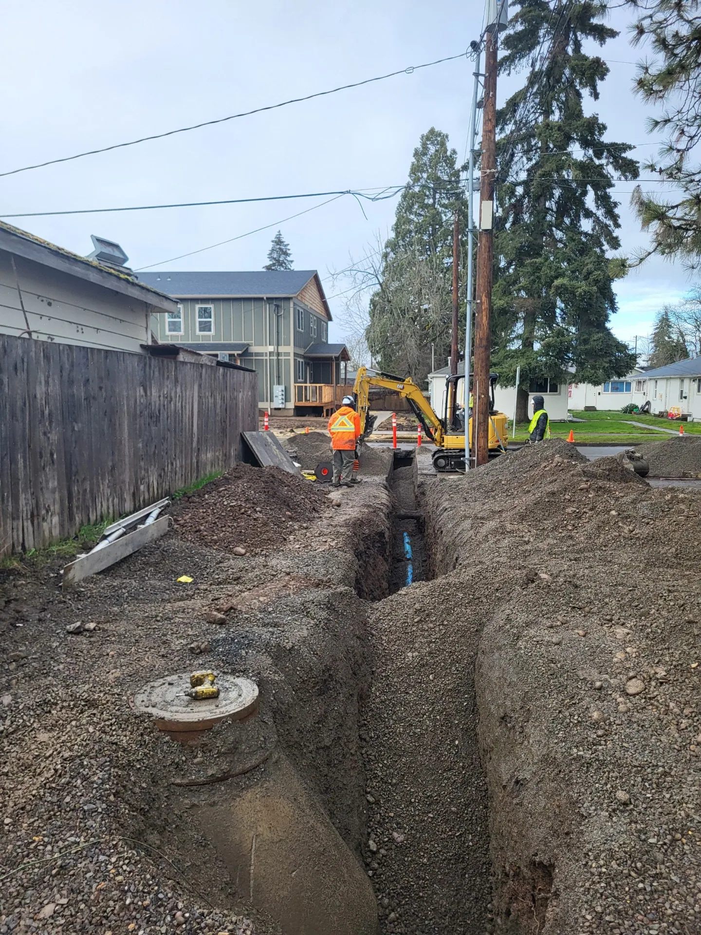 Trench along a fenced alley to a buried line, with a capped riser in front