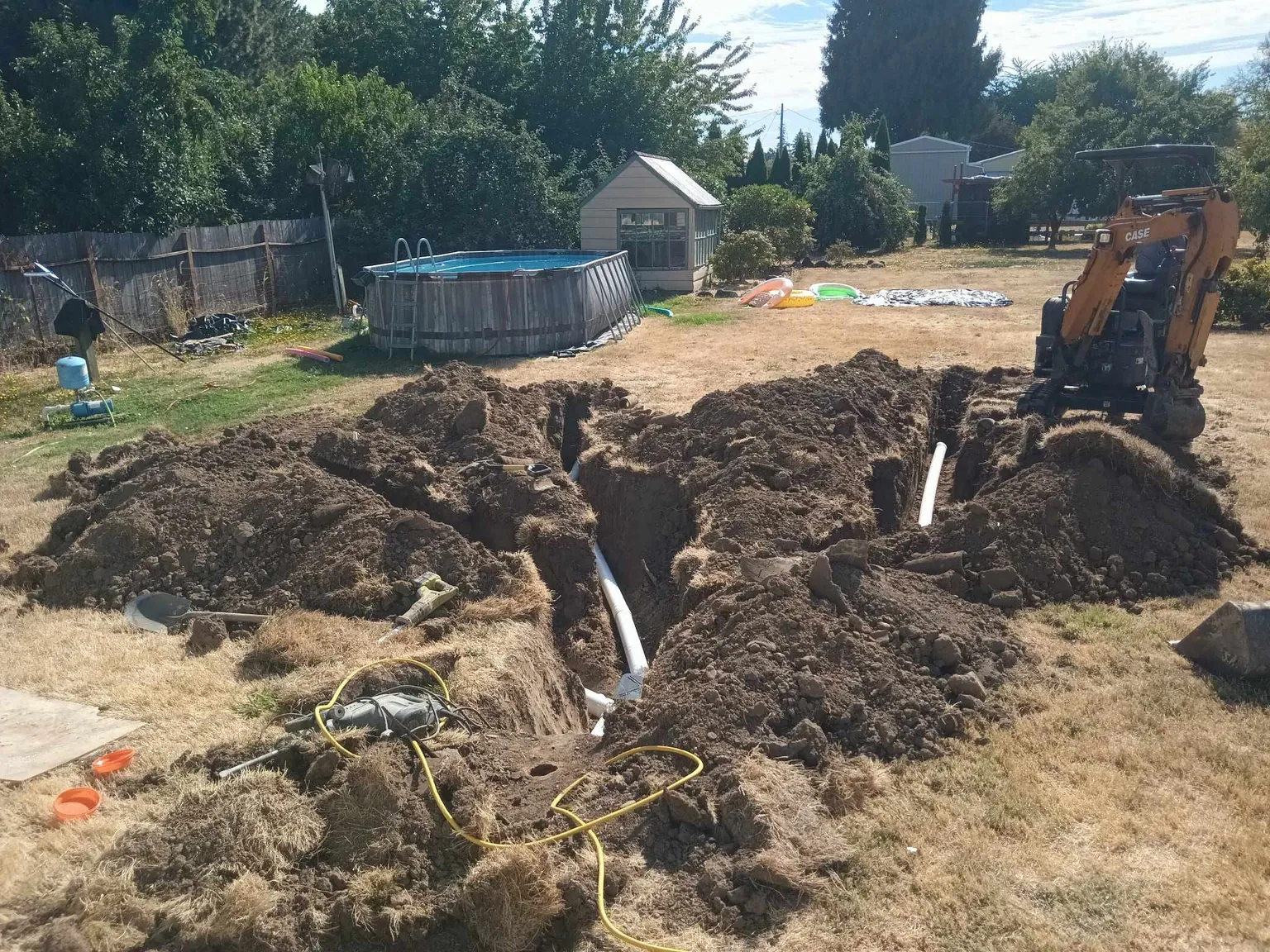 Backyard dug open to reach a buried pipe, with a mini excavator working