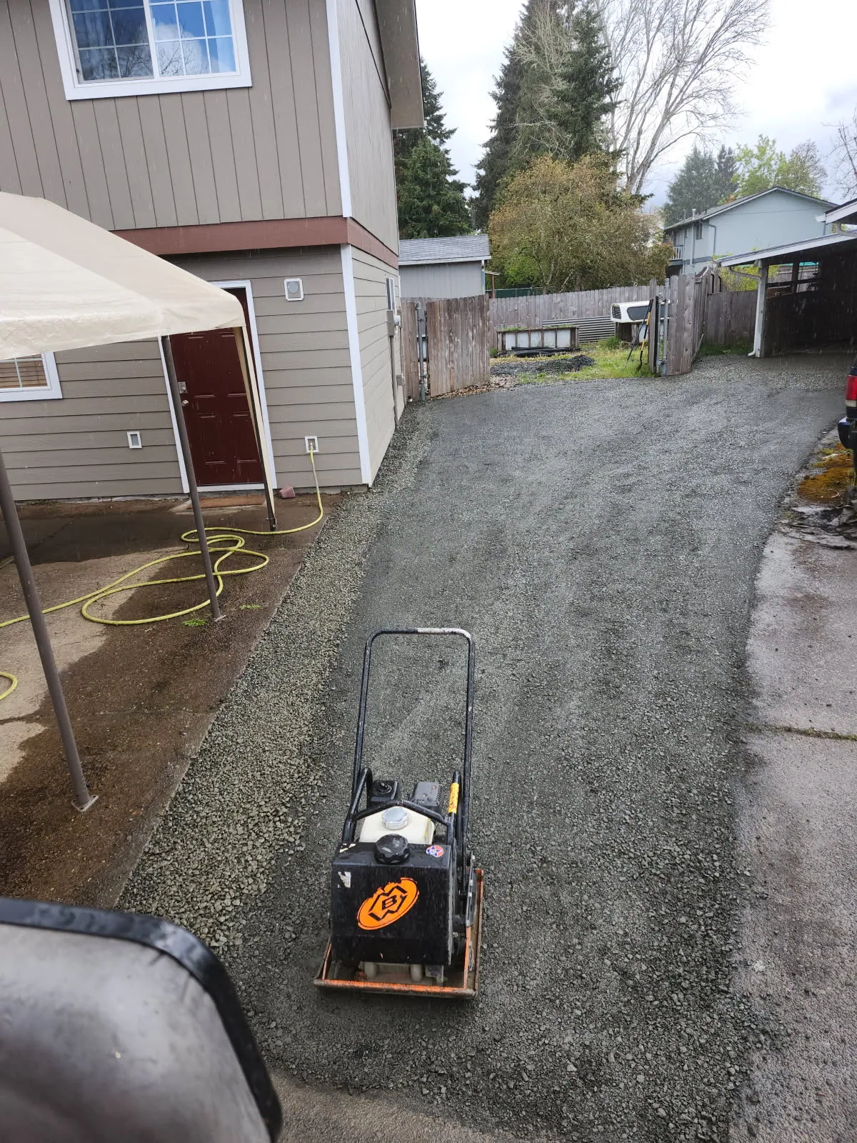 Fresh gravel being compacted along a side yard after the pipe went in