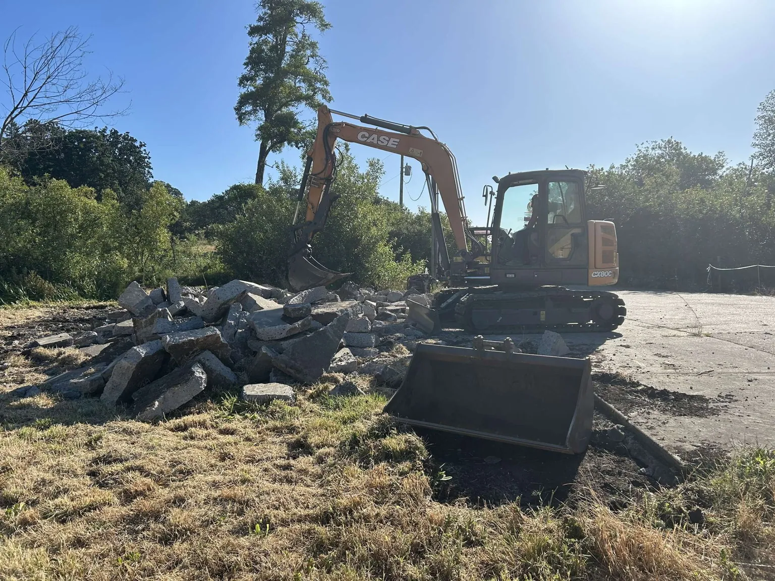 Excavator clearing a pile of broken concrete from a yard