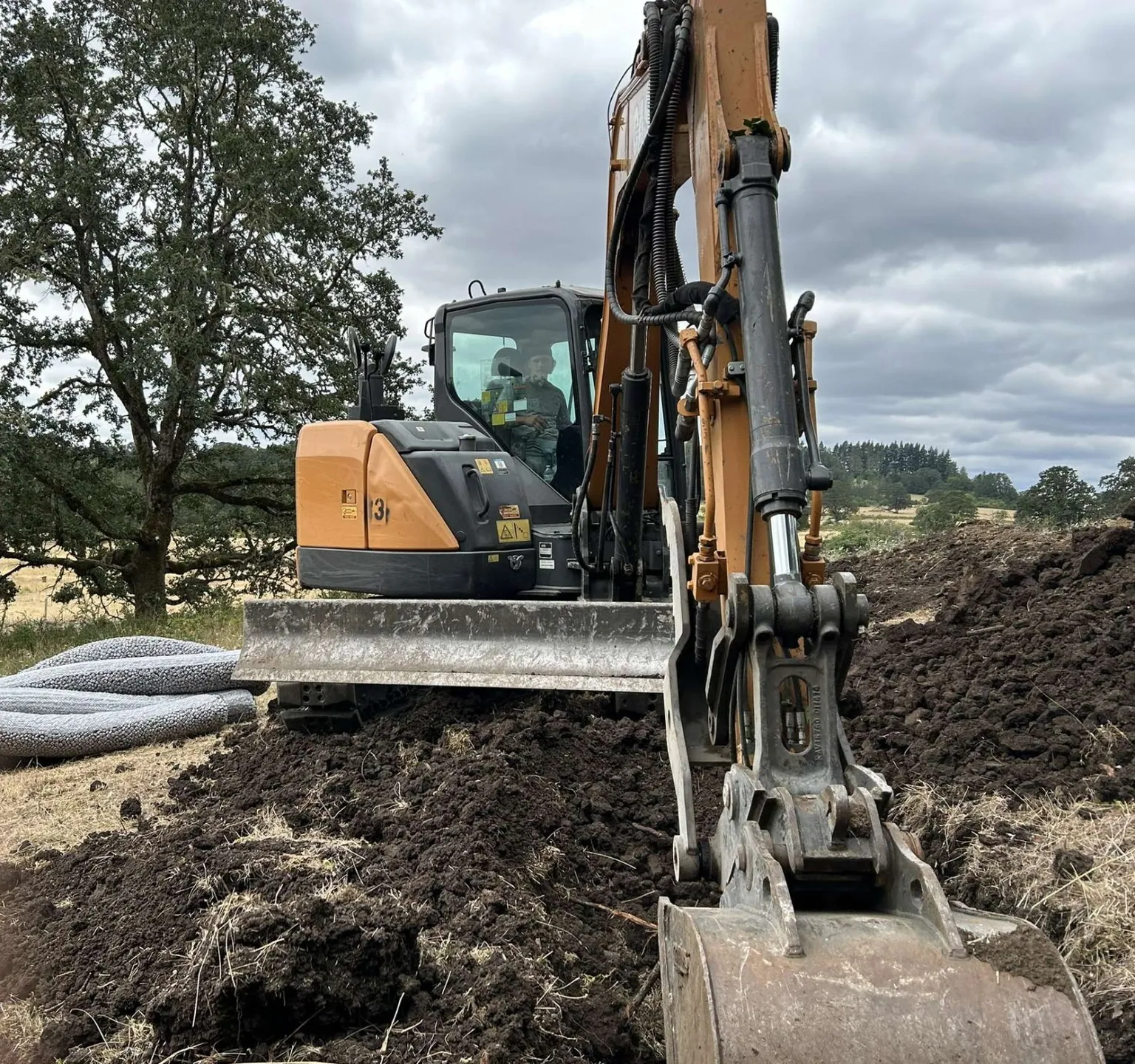 Excavator digging a trench with coils of perforated drain pipe ready