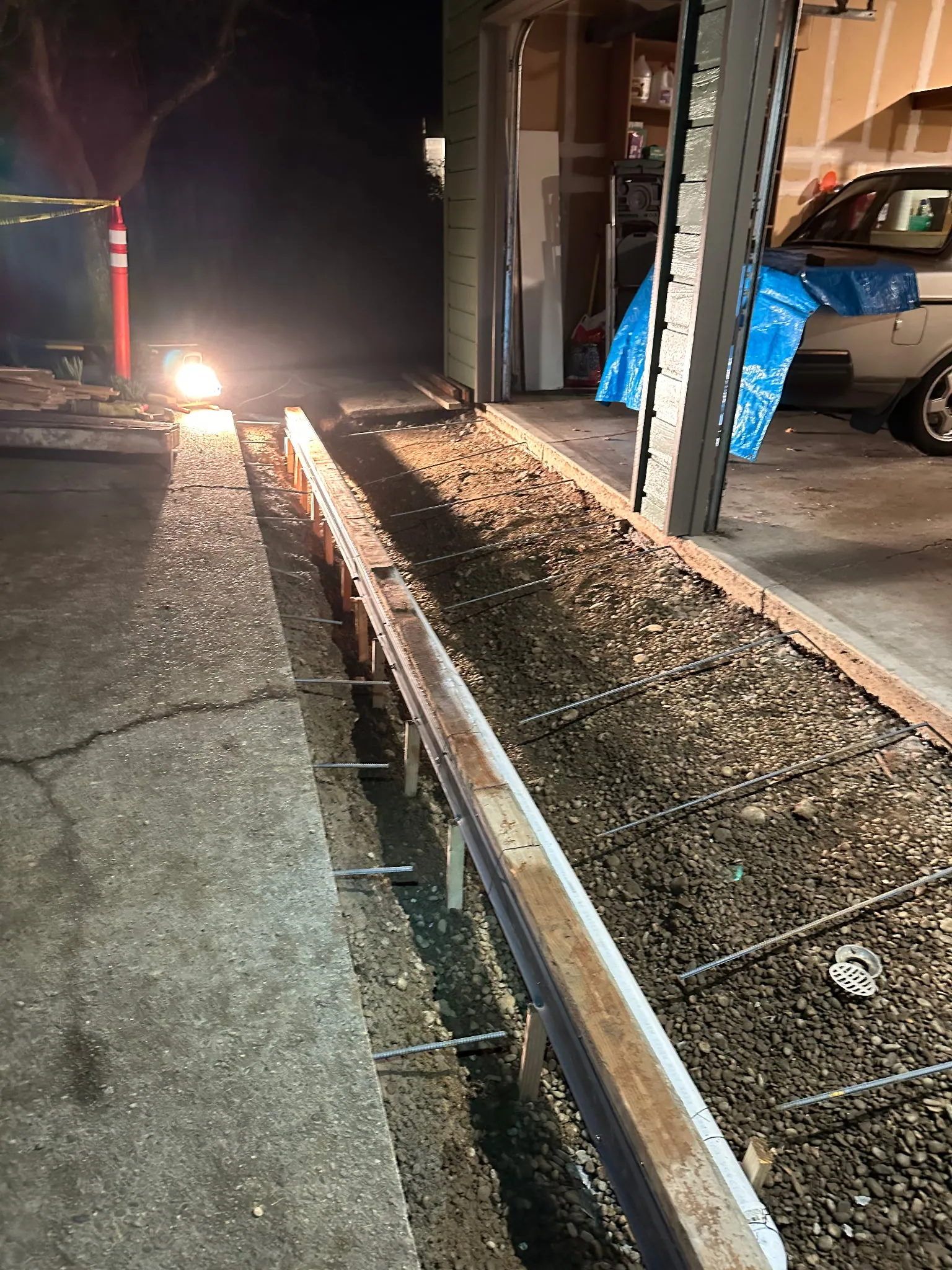 Forms and rebar set for a trench drain across a garage entry, lit for night work