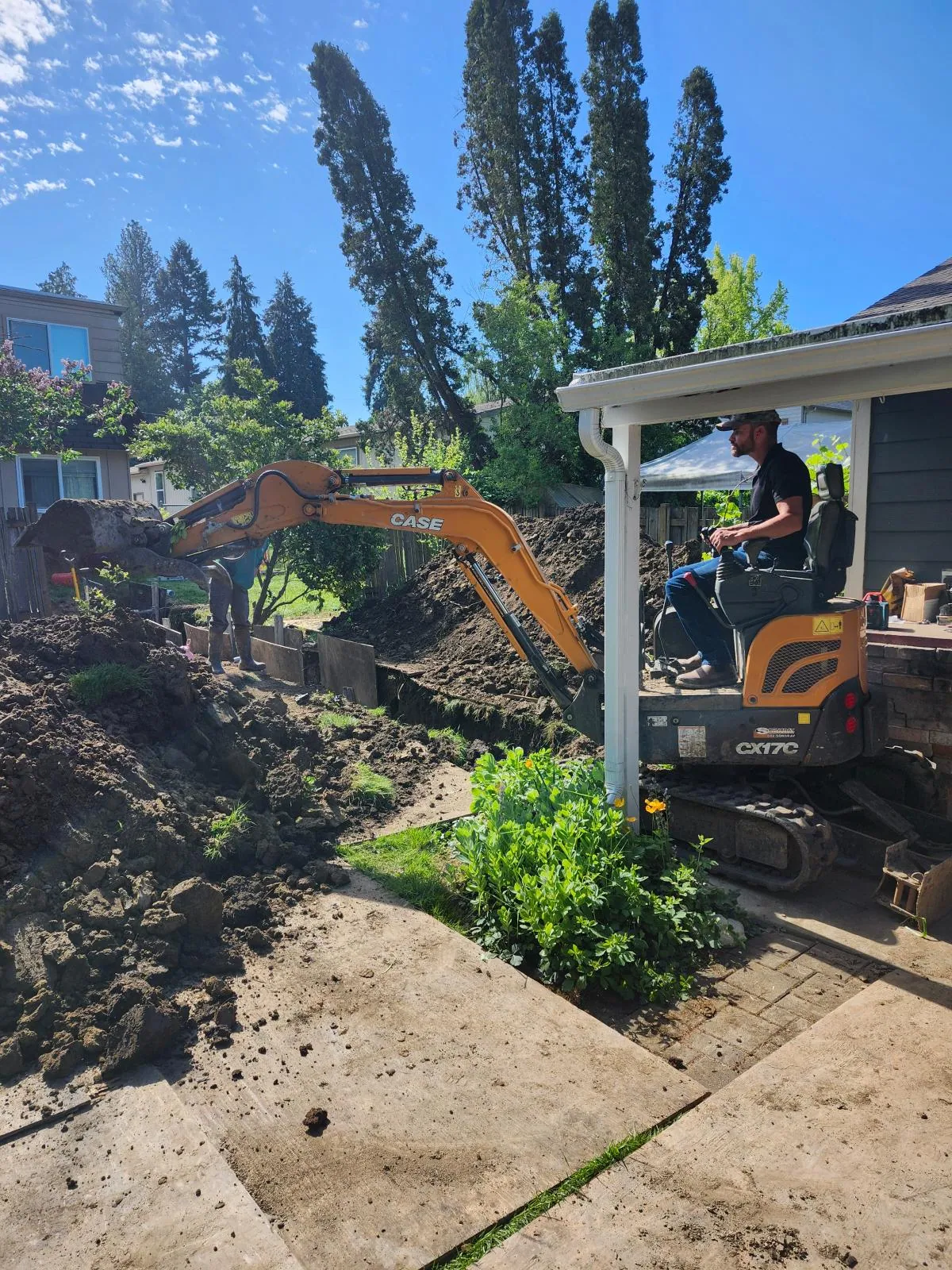 Mini excavator digging a trench beside a back patio