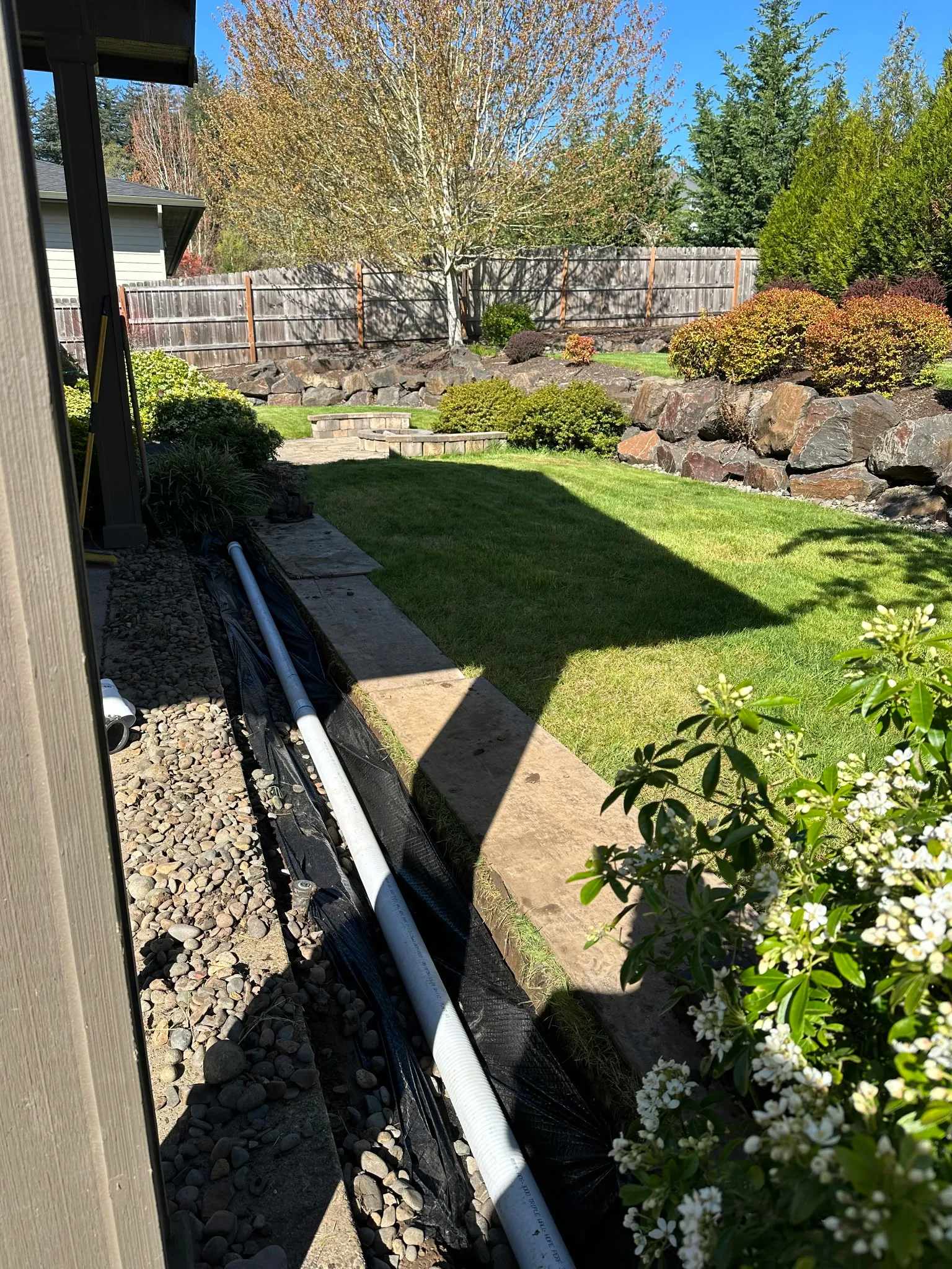 New white rain drain pipe laid in a trench along a house foundation