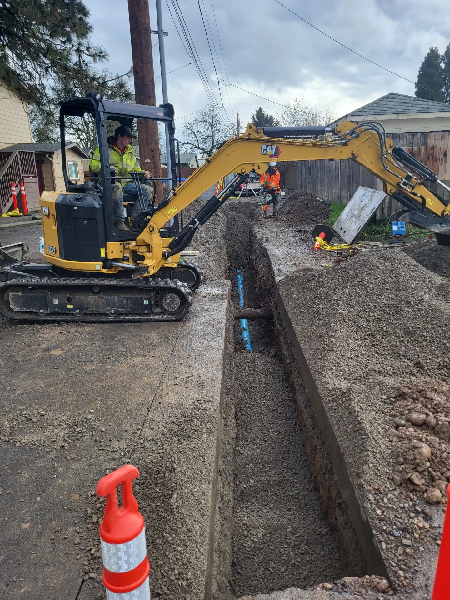 Mini excavator in a deep trench along a street, the new line at the bottom