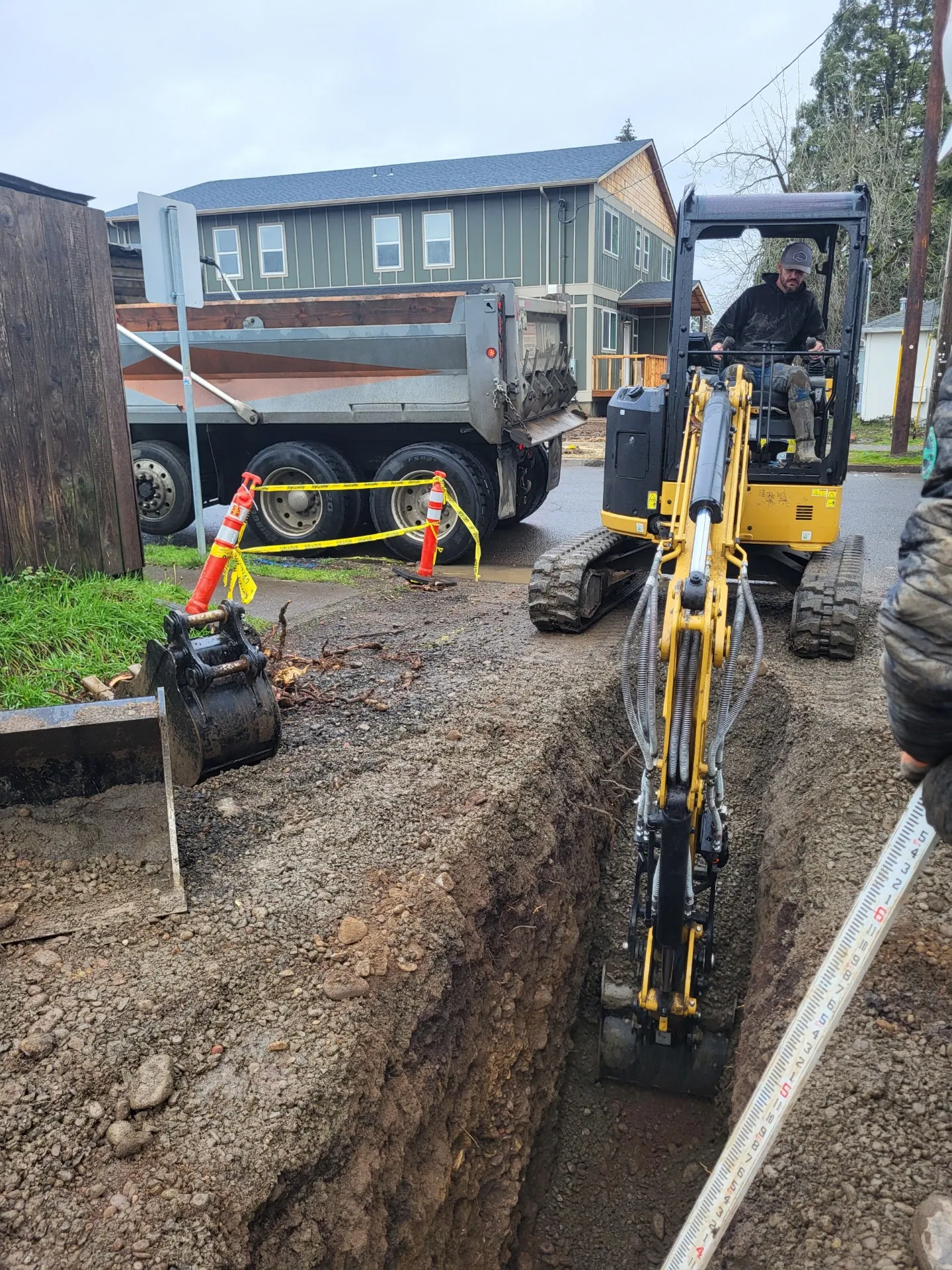 Mini excavator in a trench beside a sidewalk with safety cones set